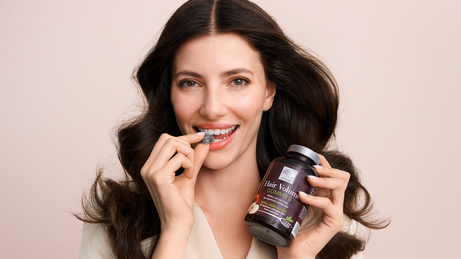 Biotin for Health Growth - Does it Work? 13 A woman holding New Nordic Hair Volume™ gummies, about to take one in her mouth.