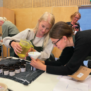 Urteskoler 28 Two women experimenting with herbs at a herbal school event, learning about and engaging with plants.