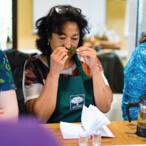 Urteskoler 30 Woman smelling herbs at a herbal school event, engaging with plants and learning about their uses.