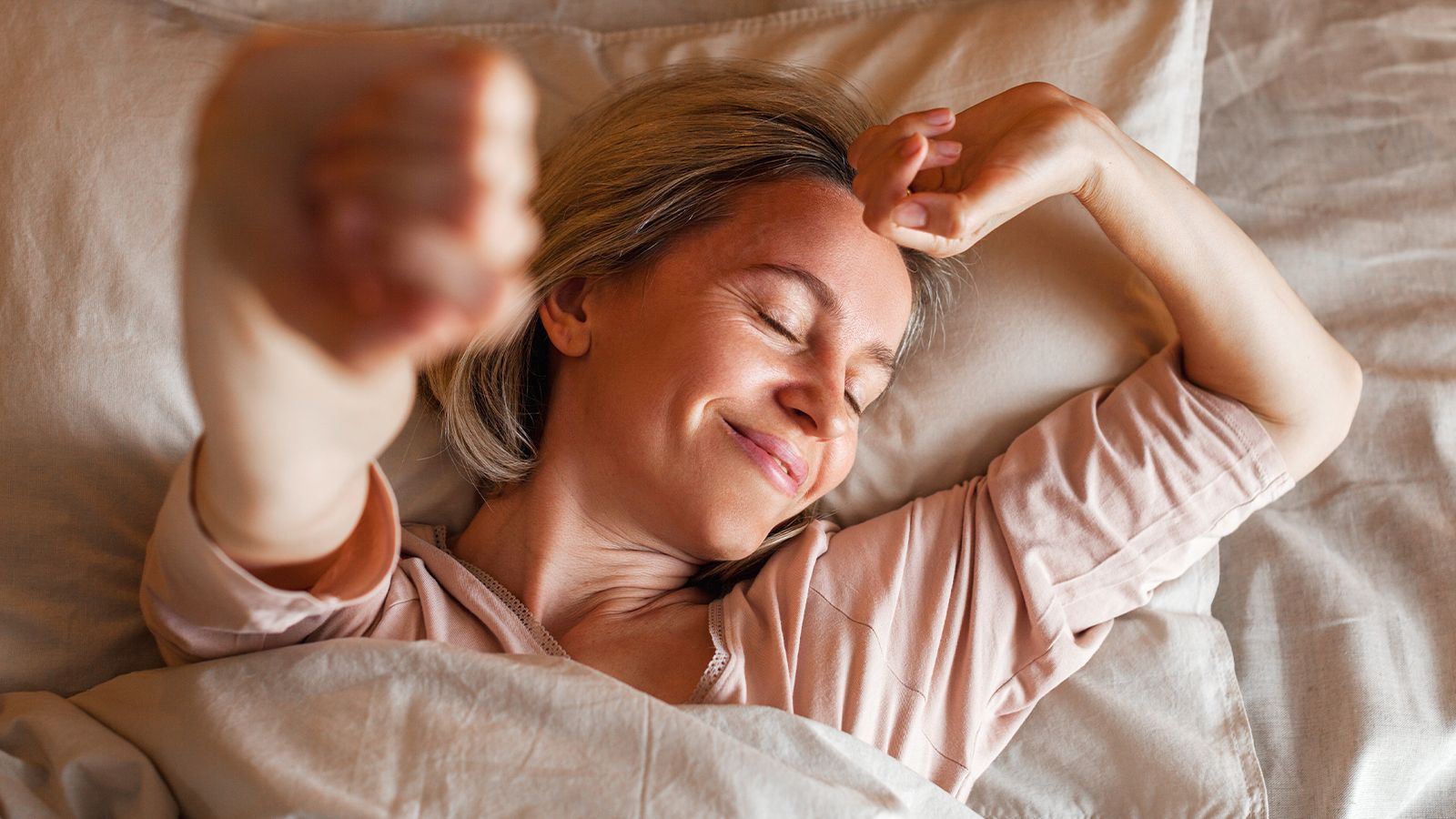 Can Magnesium Help You Sleep Better? 10 A woman lying in bed, stretching her arms and smiling, looking relaxed.